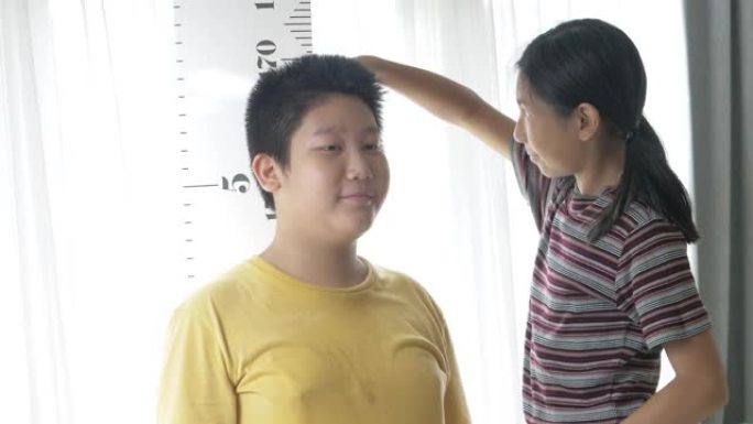 快乐的亚洲女孩在家对着窗户测量哥哥的身高，生活方式的概念