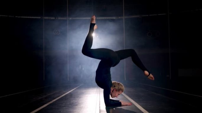 体操运动员女性在黑暗舞蹈工作室表演的剪影。灵活的女人
