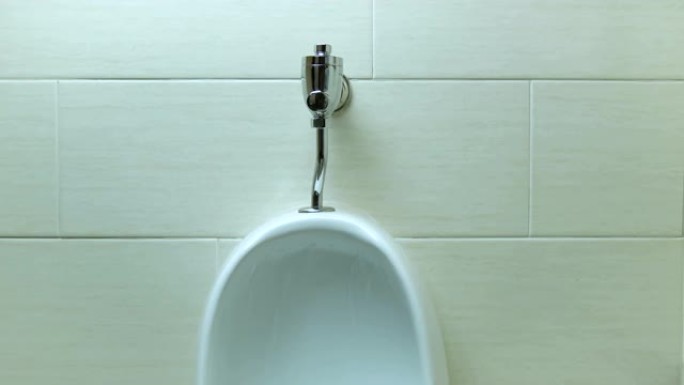 用手按下陶瓷小便池按钮冲洗尿液。