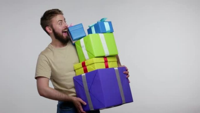 快乐的大胡子家伙庆祝生日，走路，小心翼翼地拿着许多礼品盒，看着相机