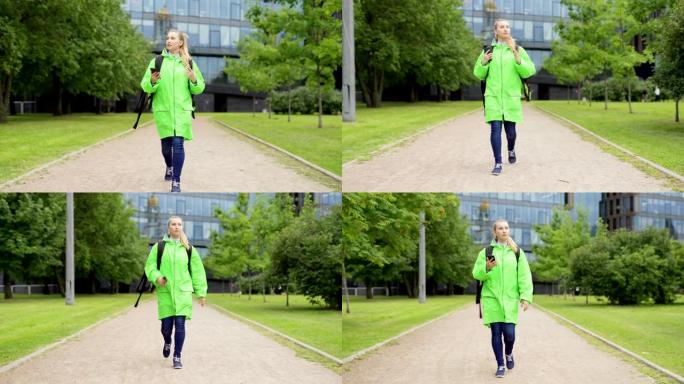 穿着绿色制服和保温袋走在街上的十几岁女性食品快递员的全长前视镜头，在智能手机上使用全球定位系统应用程