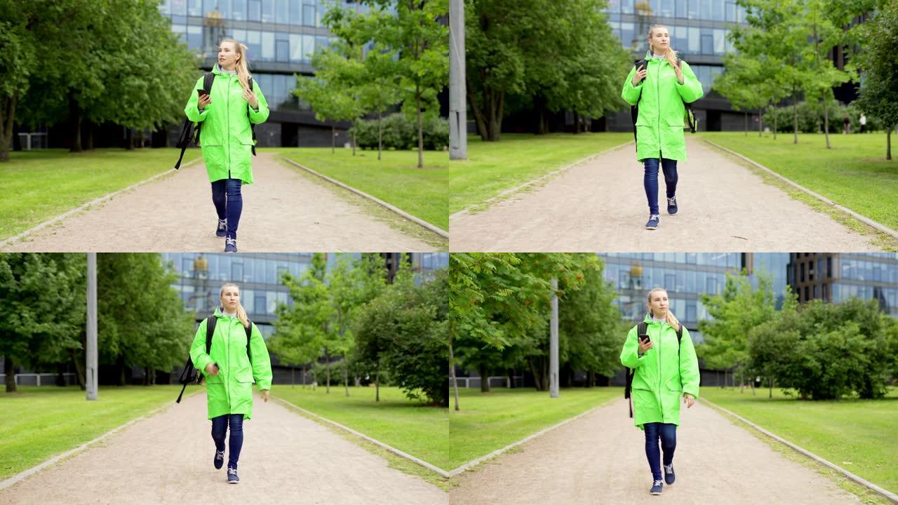 穿着绿色制服和保温袋走在街上的十几岁女性食品快递员的全长前视镜头，在智能手机上使用全球定位系统应用程