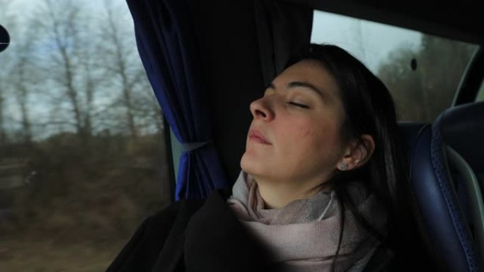 女乘客在公路上旅行时在公共汽车上睡着了。睡在公共汽车窗户旁边的女孩