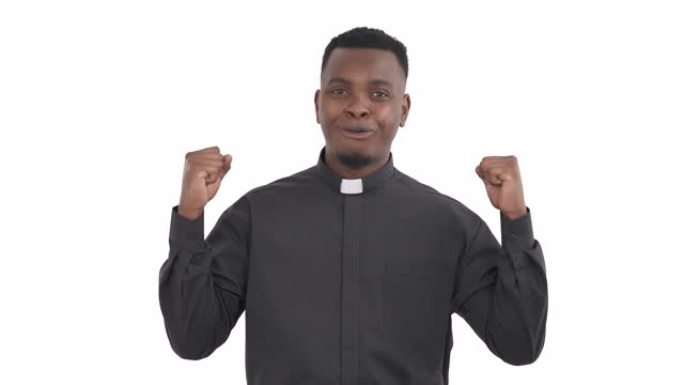 快乐的黑人牧师的肖像举起双手和拳头，呼吸着白色背景上孤立的缓解迹象。拳头泵标志