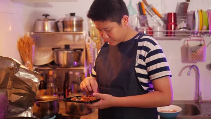 亚洲青春期男孩用发光二极管灯在厨房为家庭准备食物。