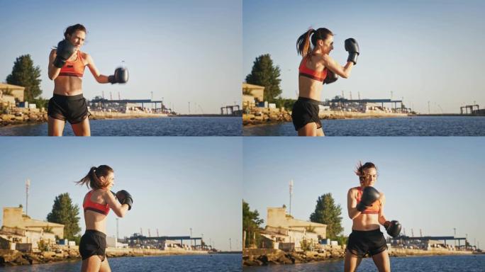 穿着拳击手套和运动服的年轻女孩在城市港口附近的海边训练时正在拳击。夏季早晨慢动作