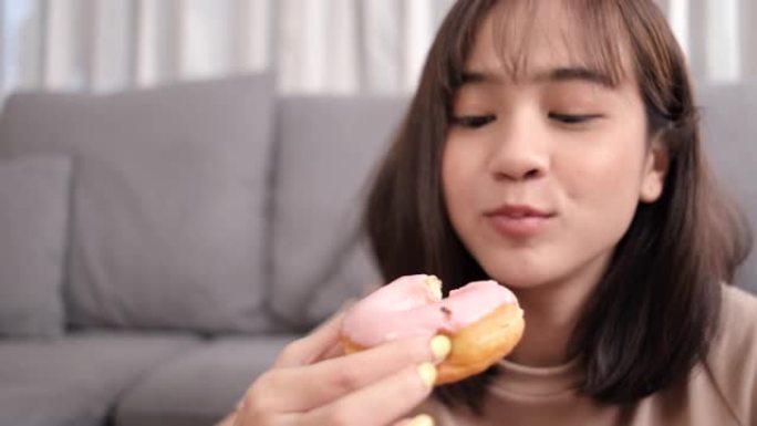 关闭亚洲女性外卖吃甜甜圈甜垃圾食品，女性在客厅享受乐趣的反式脂肪，快餐提供服务安全，阻止冠状病毒因社