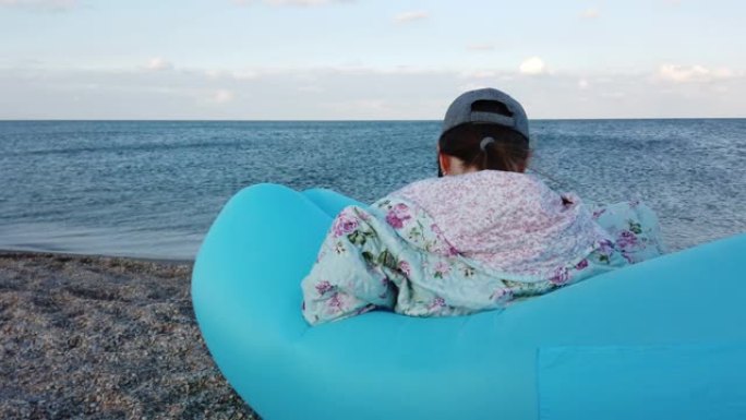 海滩上的一个女孩坐在充气吊床上。