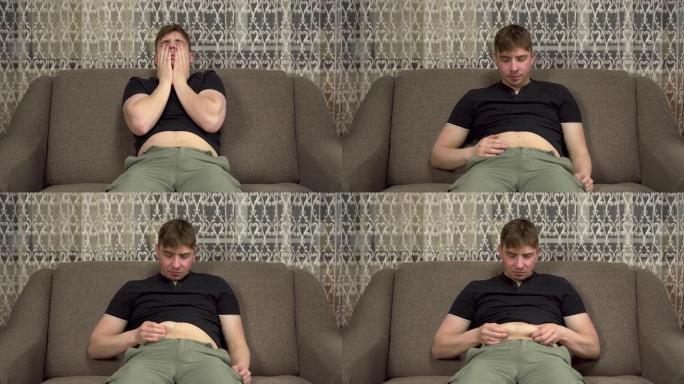 一个年轻人坐在沙发上，在肥胖的肚子上打屁股。在检疫中增加了多余的体重。