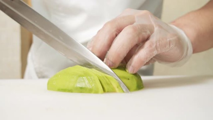将男厨师的手放在手套上，将成熟的鳄梨水果切成白板。