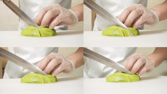 将男厨师的手放在手套上，将成熟的鳄梨水果切成白板。