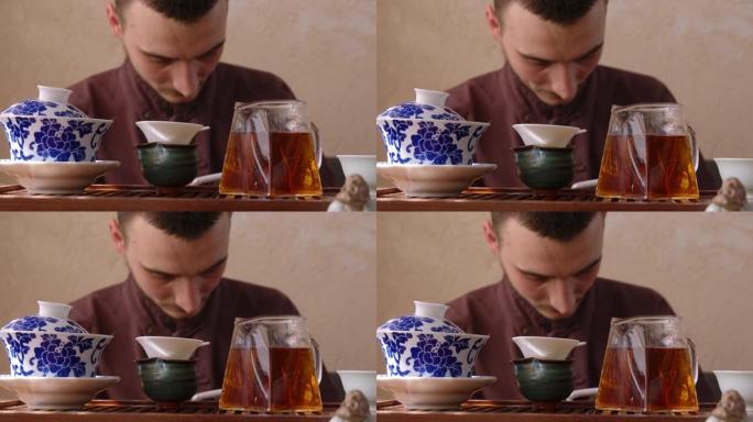 年轻人在东方餐厅茶道时使用手机。大师在茶几背景上用智能手机聊天，配有玻璃公平投手、筛茶碗和盖碗。