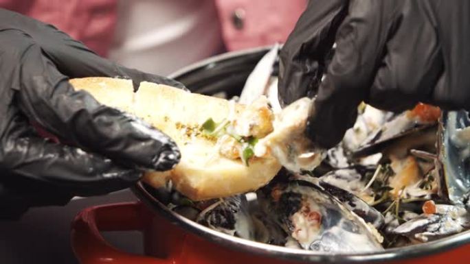 双手戴着黑手套的特写镜头，将贻贝和奶油酱放在吐司上。地中海美食。