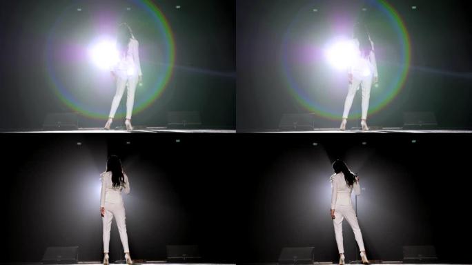 美丽的歌手在白色聚光灯下的黑暗中在舞台上唱歌