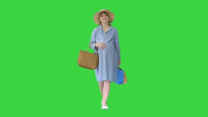 穿着夏装的孕妇带着购物袋走在绿屏上，色键