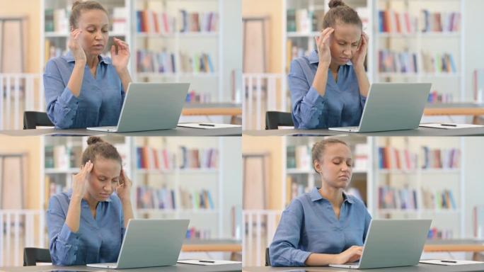 紧张的非洲妇女笔记本电脑在图书馆头痛