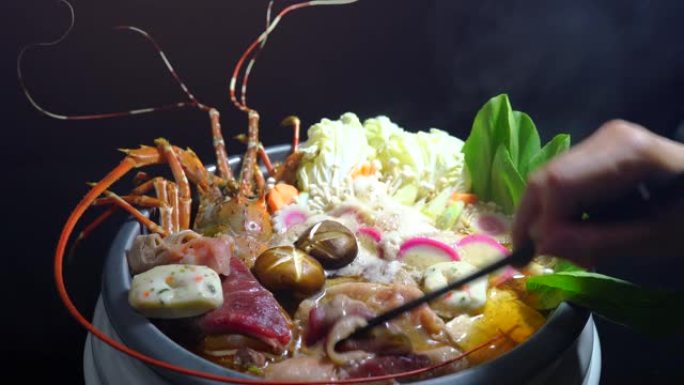 寿喜烧多刺龙虾与蔬菜和肉类一起在火锅中食用，多刺龙虾Nabe，用筷子将肉放入火锅中。