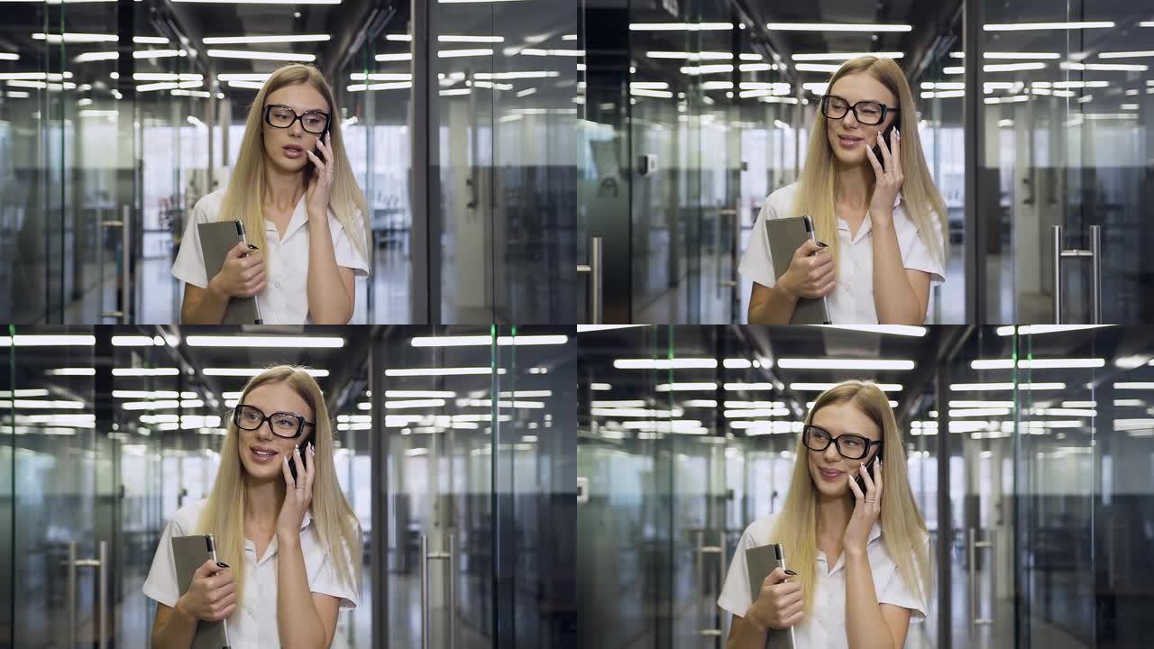 戴着眼镜的灿烂微笑的高超女商人的前视图，当走过办公室走廊时在电话上交谈