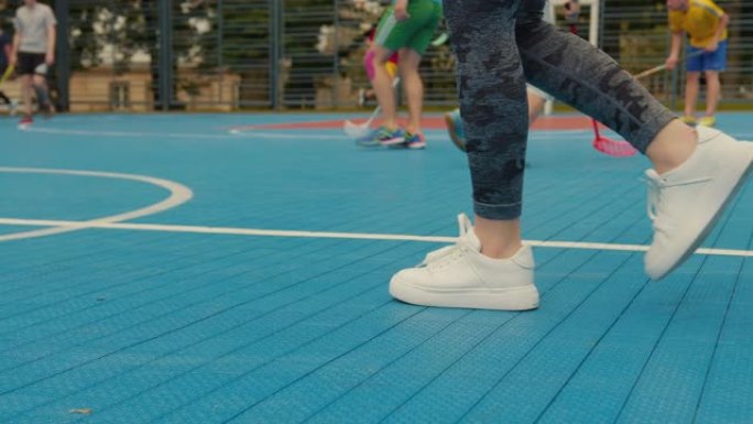 一个女孩的腿的特写。一个女孩在篮球场上走着。背景是人们在打地板球。4 k
