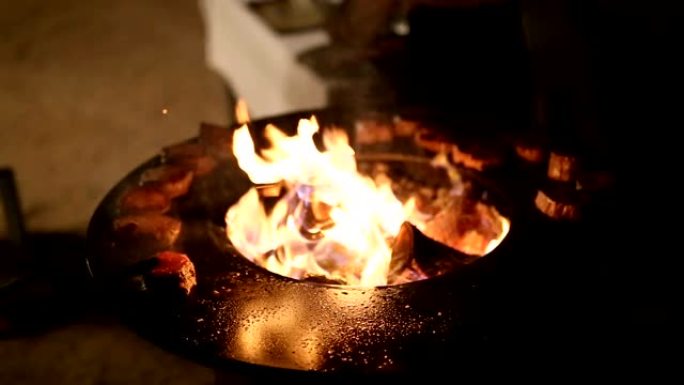厨师用钳子将肉排放在烤炉上。肉牛排是在一个圆形的铁户外烤架上准备的，烤架上有一个炉灶面，中间有一个明