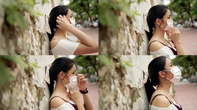 迷人的亚洲女人戴着白色防护面具，侧视背靠墙，新型冠状病毒肺炎电晕病毒，环境保护，白天，新常态，户外场