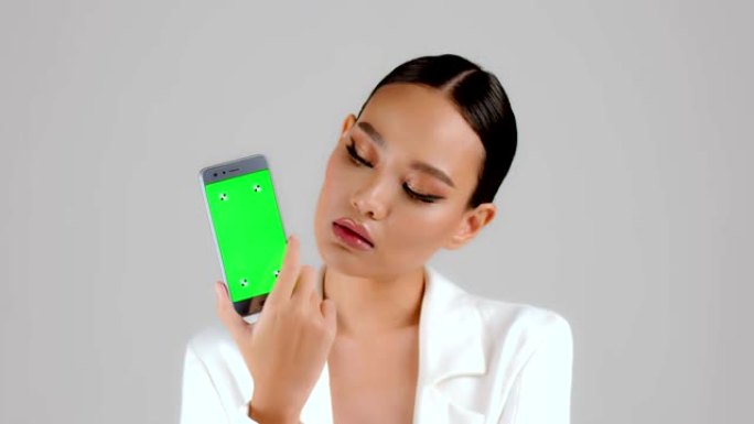 美丽的亚洲女商人展示绿屏智能手机，看着相机