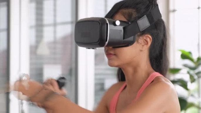 亚洲女性戴着虚拟现实耳机在家用操纵杆玩拳击练习。可穿戴技术