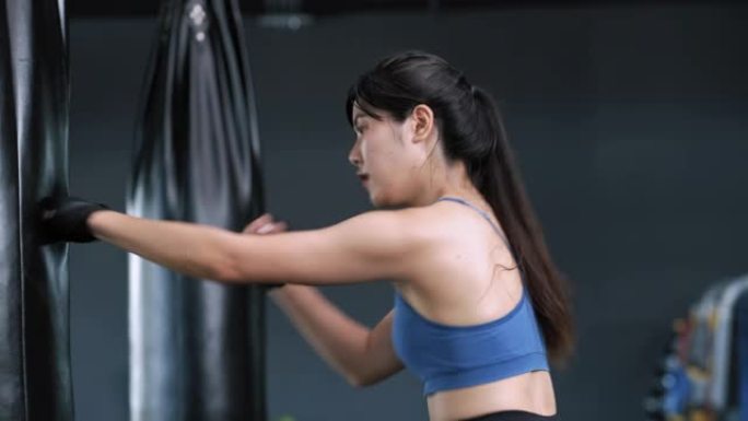 动作镜头: 运动的年轻亚洲女拳击手戴着腕带，穿着运动服的女人准备拳击练习或锻炼。运动员适合健身房训练