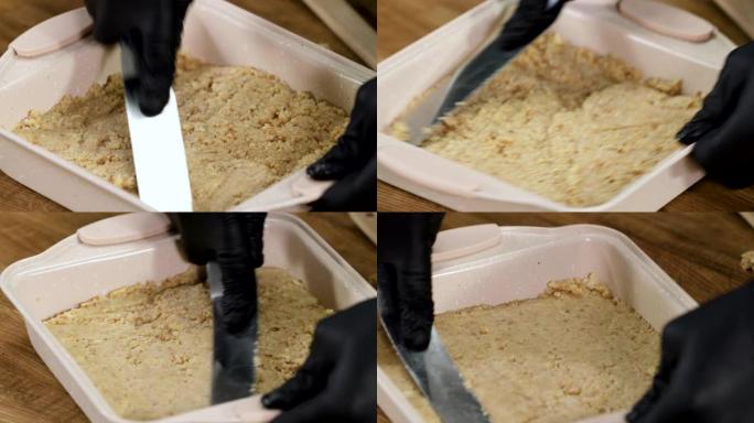 专业厨师做芝士蛋糕。戴着黑色手套的男性手，用抹刀在烤盘中撒上磨碎的饼干。4K