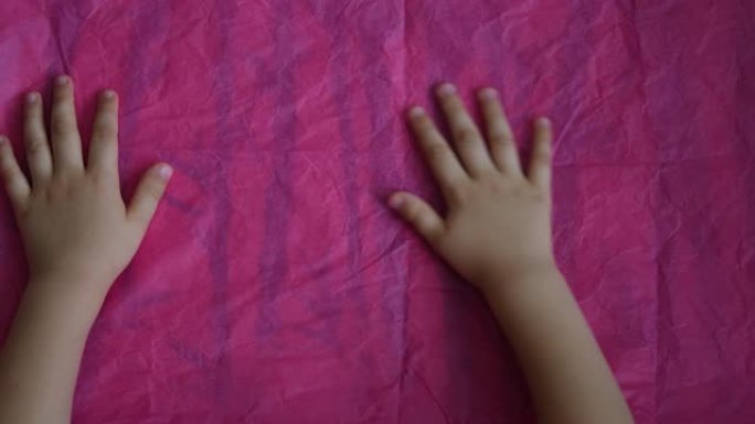 儿童手的俯视图在桌子上的粉红色皱巴巴的纸上，有复印空间