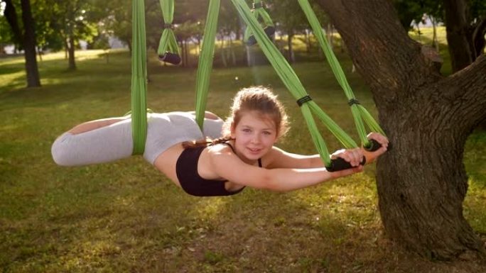一个小女孩正在树园做飞行瑜伽。一个孩子在吊床上做瑜伽。