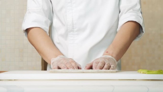 男厨师双手合十，用手套在厨房里铺上竹垫做寿司。