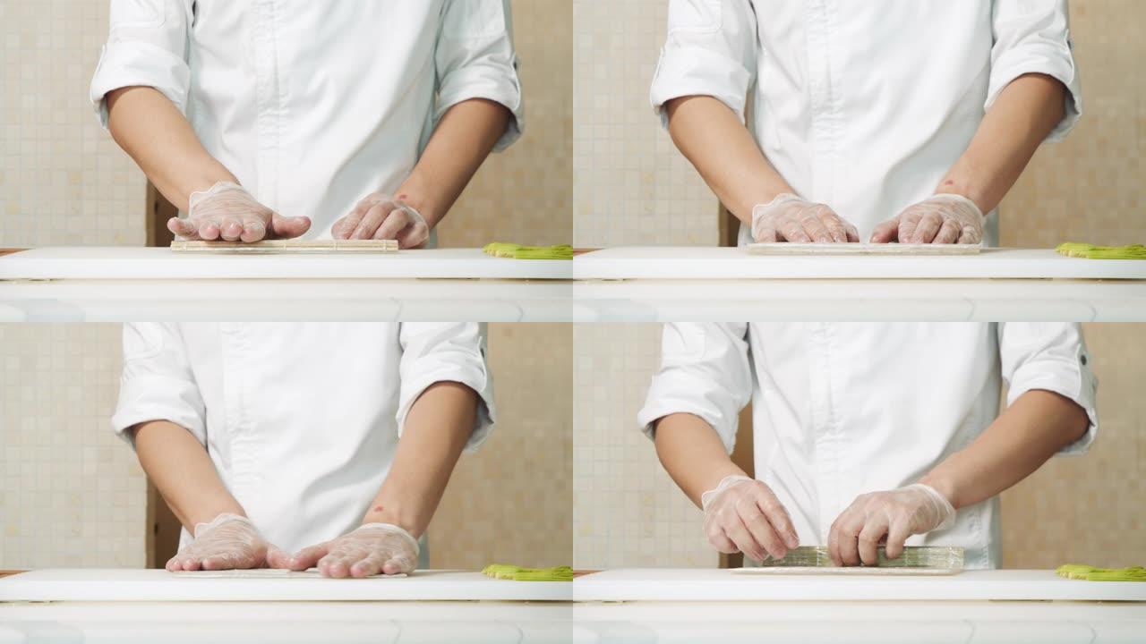 男厨师双手合十，用手套在厨房里铺上竹垫做寿司。
