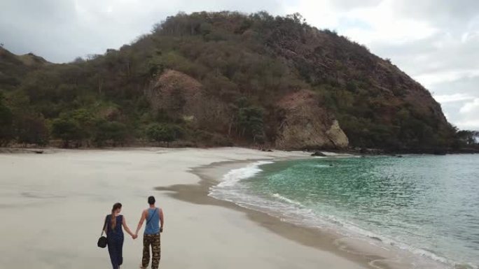 夫妇牵着手走在田园诗般的科卡海滩上。印度尼西亚弗洛雷斯的隐藏宝石。夫妇正在享受他们浪漫的逃亡。波浪轻