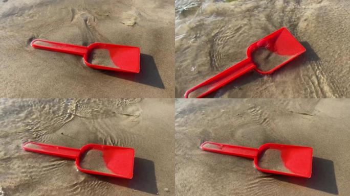 红色的刮刀躺在沙子上，移动波浪