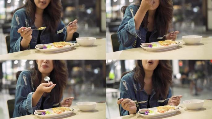 年轻的亚洲妇女坐在自助餐厅吃饭。美丽的亚洲女孩独自吃饭
