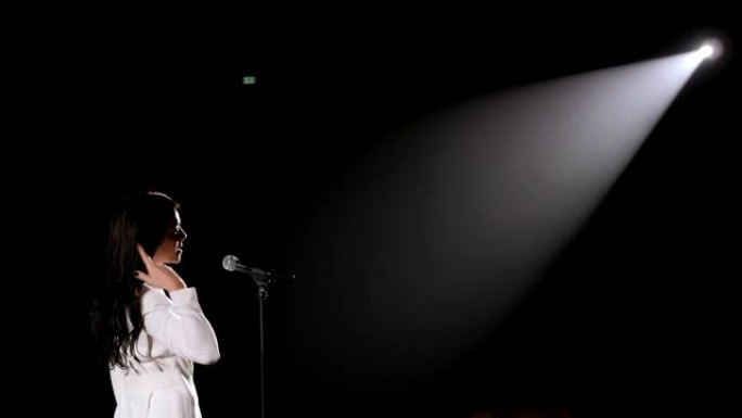 一位美丽的歌手在白色聚光灯下的黑暗中登台。