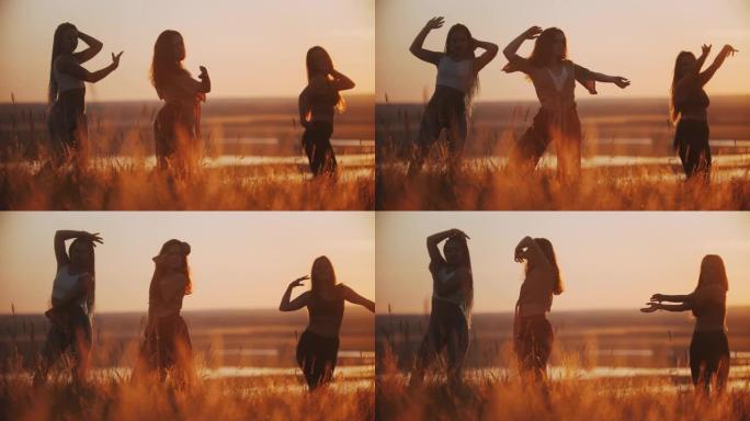 三个年轻女子在做有氧舞蹈和缓慢的动作，他们的手在日落