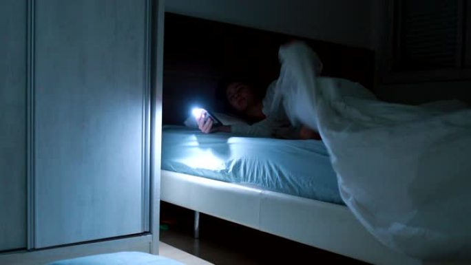 女人在半夜用手机手电筒躺在床上寻找东西