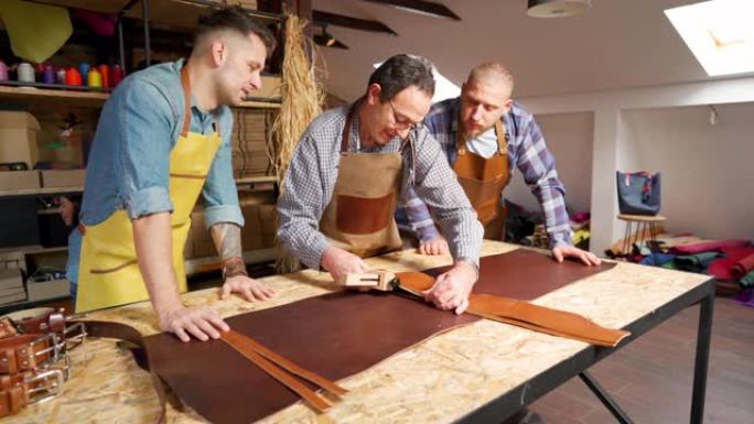 高级工匠向他的两个年轻同事展示如何在车间切割皮革材料
