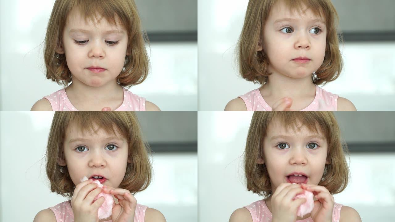 特写小可爱3岁的小女孩吃甜美的粉红色棉花糖，看着相机，微笑着笑。