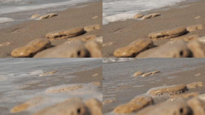 有石头的沙滩上有泡沫的海浪。海石覆盖着波浪。慢动作。