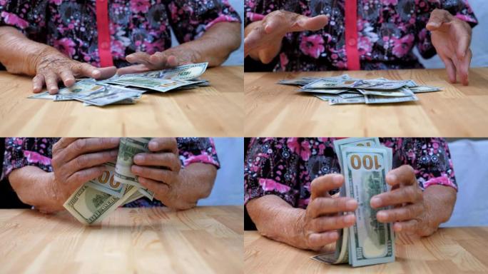 皱巴巴的女性双手从桌子上拿出一堆堆的外币。祖母的手臂从桌子上耙出散落的100美元钞票。低视野慢动作