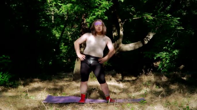 富有表现力的超重男人，长发，穿着有趣的女性衣服在森林里健身。顽皮的胖子描绘女孩做减肥体操。