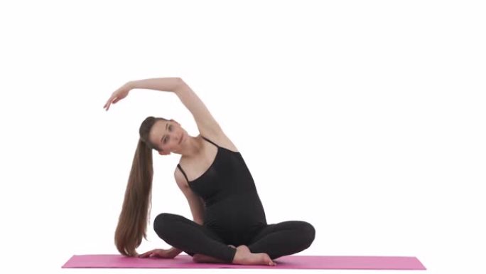 瑜伽训练。白人孕妇以蝴蝶姿势坐在垫子上，做上半身侧伸展。孤立在白色背景上。