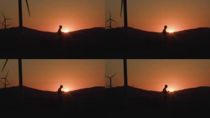 工程师在平板电脑上写下信息，看着日落时的风车。剪影拍摄。环保能源的概念
