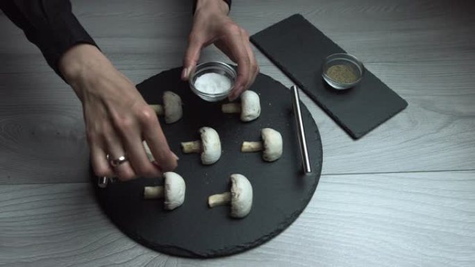 手指上有美丽修指甲的女性手为蘑菇，盐和胡椒粉，黑板，特写。钱皮农。女人在家准备晚餐