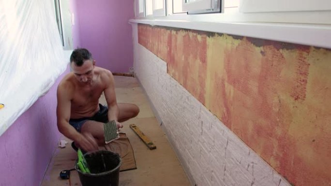 一个蹲下的人正在凉廊的墙上铺瓷砖。