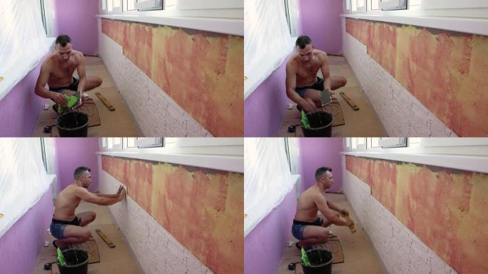一个蹲下的人正在凉廊的墙上铺瓷砖。