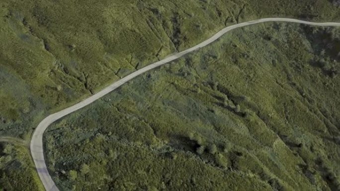 Pan拍摄了一条弯曲的道路，该道路建在被岩石和绿色植物包围的山上